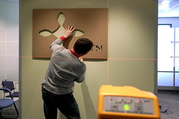 Art Signs company installers positioning lobby signage pattern of business logo on reception area wall