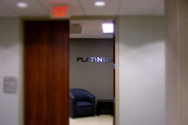 Shiny raised metal lobby signage lettering made by Art Signs Company wall mounted above chairs in reception area waiting room seen through company office door