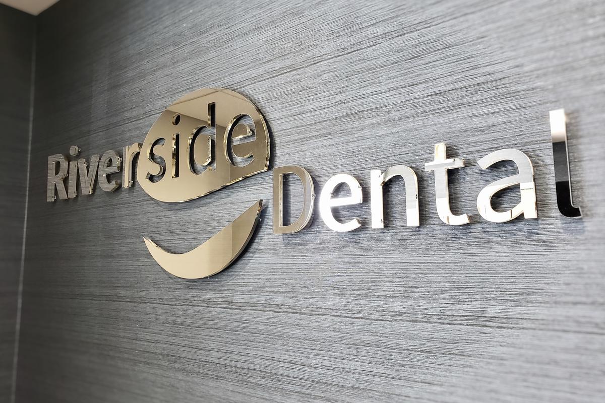 Mirrored acrylic logo sign wall mounted in dental office waiting room at Riverside Dental