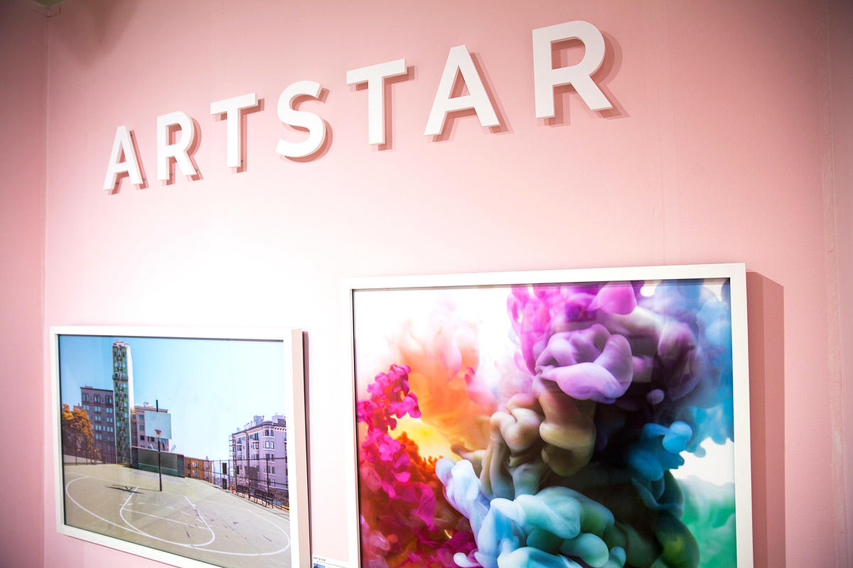Raised plastic sign letters at art show with pink walls, mounted above white framed paintings.