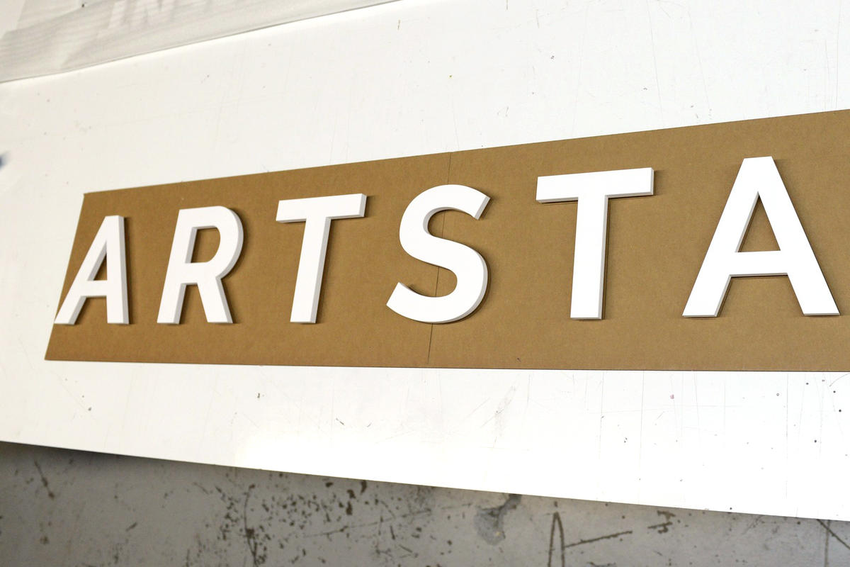 White 3D sign letters that say ArtStar laid out on brown paper cardboard pattern