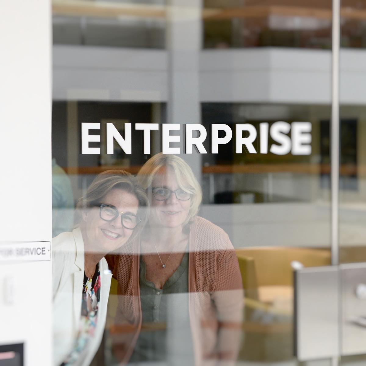 Happy customers smiling looking through door with 3D "Enterprise" letters mounted to it