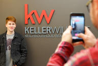 Man stands next to red Keller Williams Neighbourhood Realty front desk reception area logo.