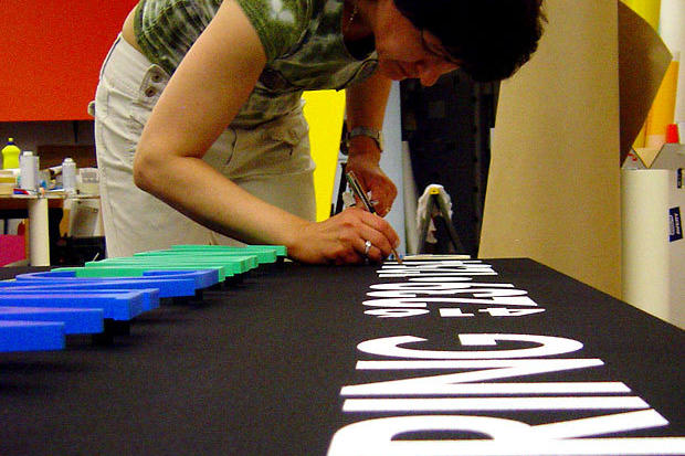 Sign installers working on custom lobby sign and vinyl decal lettering for retail business