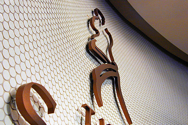 3D office reception sign logo made with dimensional copper metal letters and symbols laser cut and mounted raised off the wall on risers.
