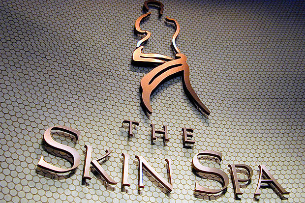 Shiny laser cut 3D copper metal lobby sign with letters and logo in skin care spa behind office reception desk.