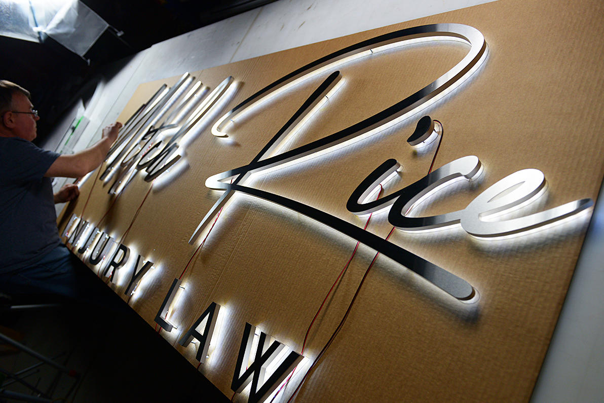 A skilled ArtSigns craftsman carefully installing an illuminated custom 3D sign with precision backlit lettering for a luxury law firm. This high-end, Canadian-made signage features sleek, polished metal and LED lighting, ensuring a bold and professional look.