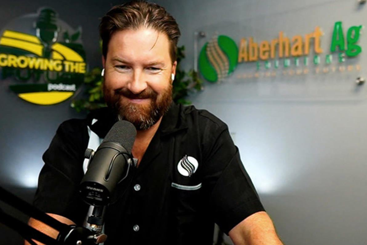 Dan Aberhart, host of Growing the Future podcast, sitting in front of two custom signs made by ArtSigns—one for Aberhart Ag Solutions and another for his podcast—highlighting his innovative contributions to sustainable farming in Saskatchewan.