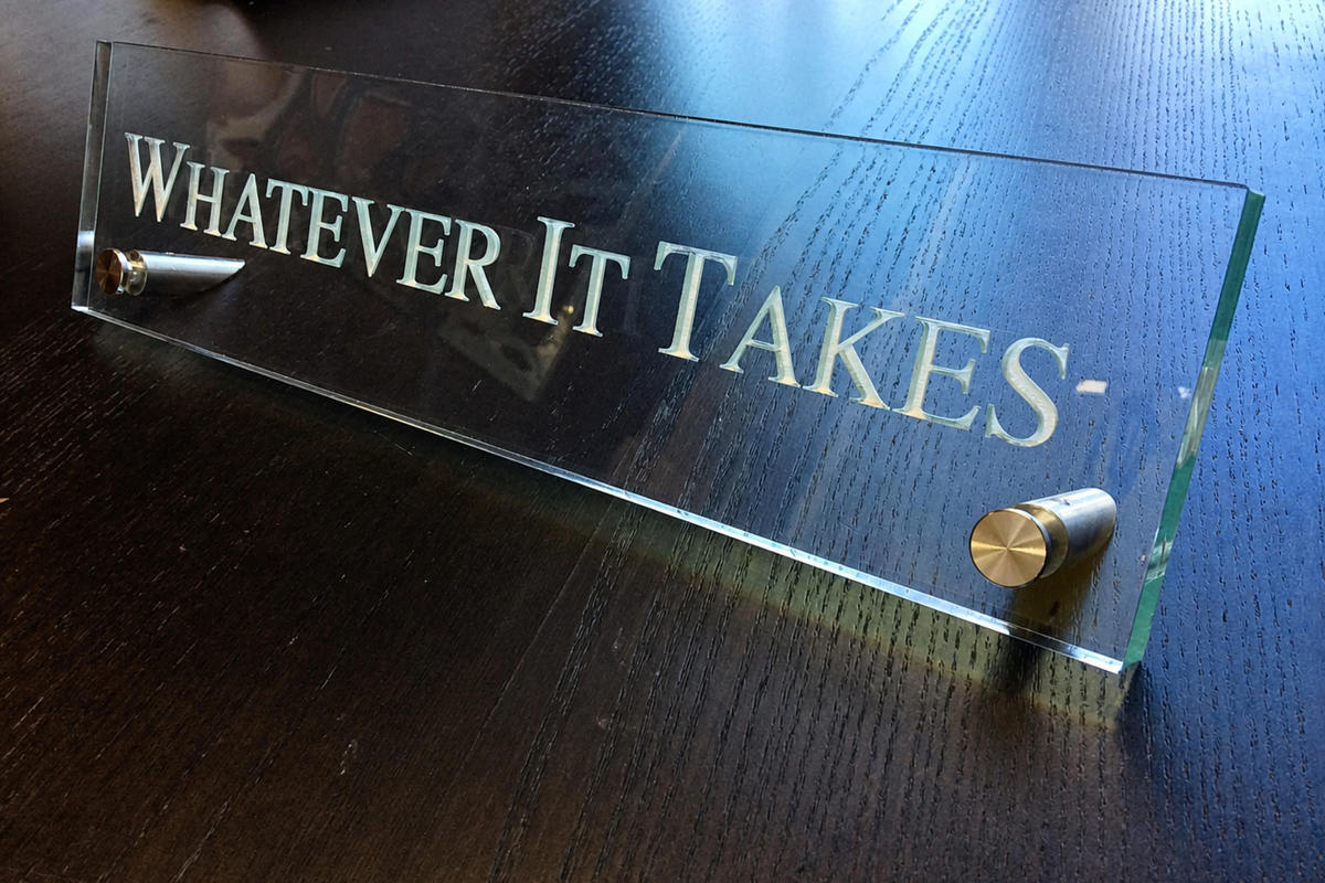 Clear acrylic desk nameplate engraved with “WHATEVER IT TAKES-” on metal standoffs