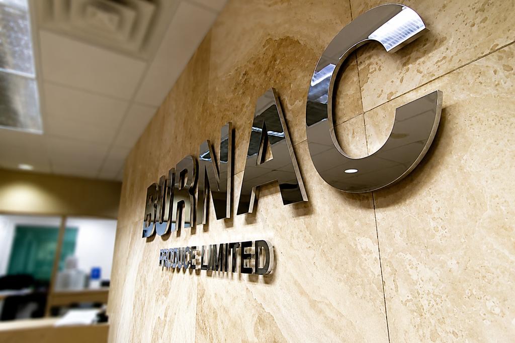 Angled view of Burnac custom 3D corporate sign made from polished aluminum on a marble office wall