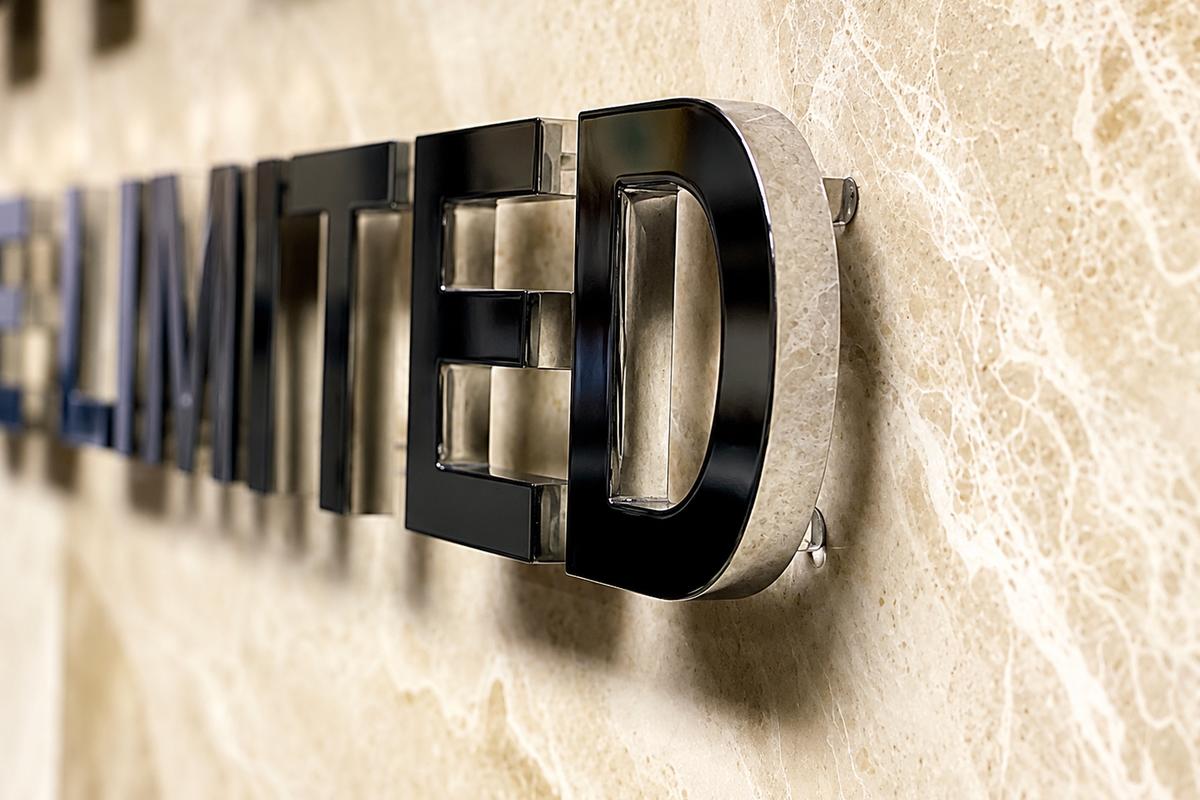 Close-up detail of mirror polished 1/2 inch aluminum dimensional letters mounted off a marble wall with clear spacers