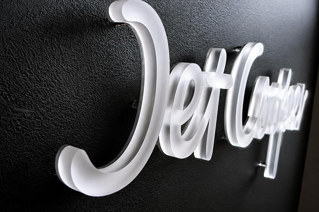 Close perspective of a frosted acrylic Jet Cooper logo showing dimensional edges and clear wall spacers.