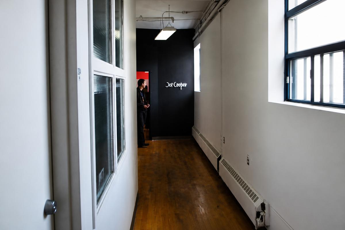Jet Cooper frosted acrylic office sign visible at the end of a bright hallway on a black feature wall