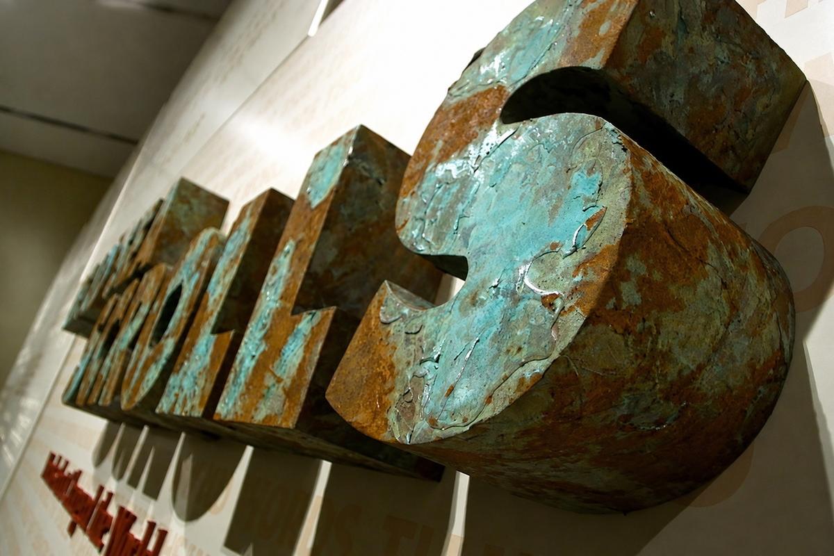 Angled close-up of thick Scrolls lettering with turquoise verdigris and rust finishes at the ROM in Toronto.