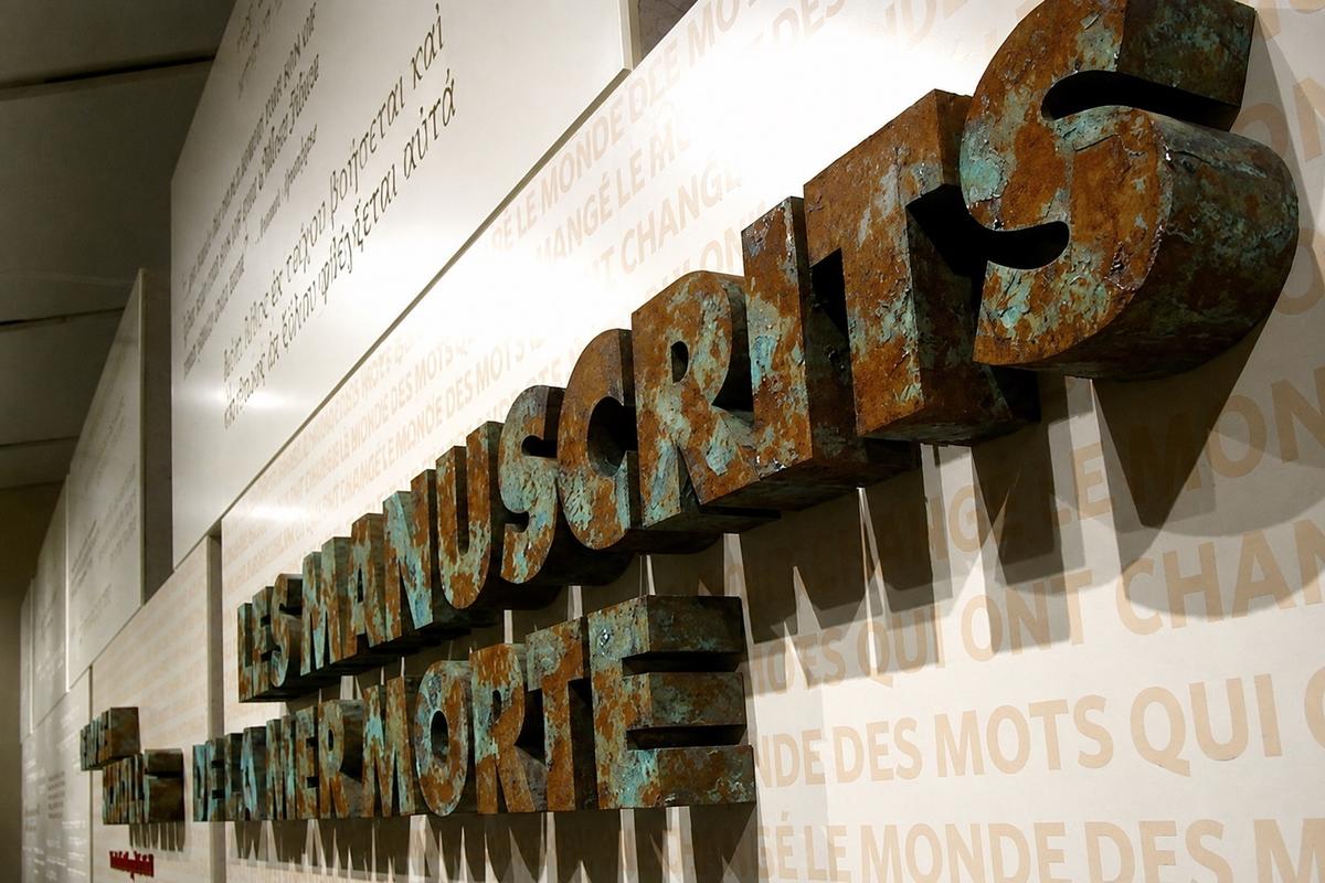 French Dead Sea Scrolls foam lettering with rust and copper patina over printed wallpaper at the ROM in Toronto.