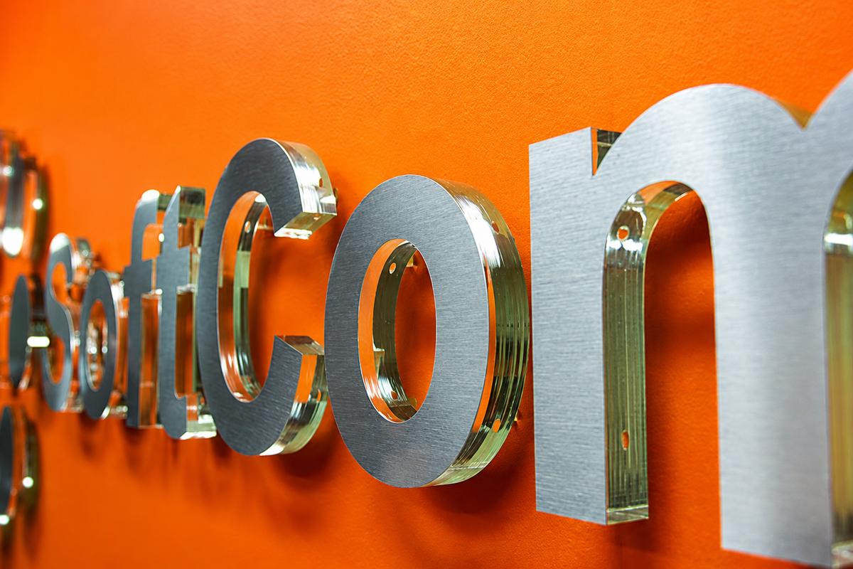 Side view of SoftCom 3D office sign with green edge acrylic, brushed metal faces, and clear spacers