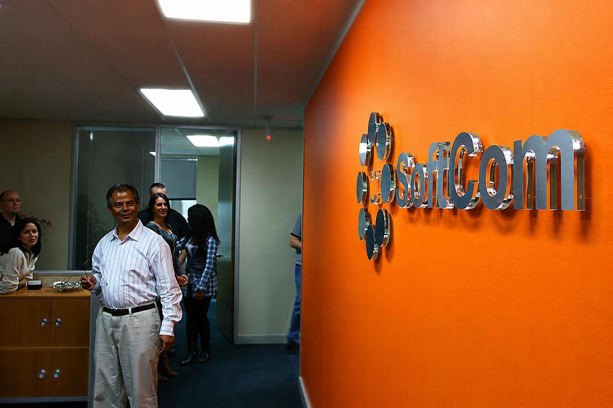 SoftCom dimensional logo sign installed on orange office wall with people in the background.