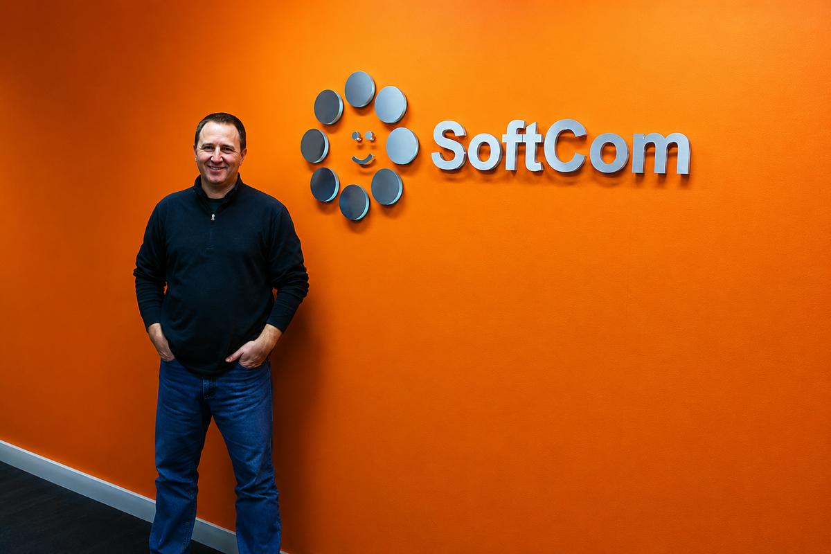 SoftCom dimensional office sign on orange wall with a person standing nearby for scale