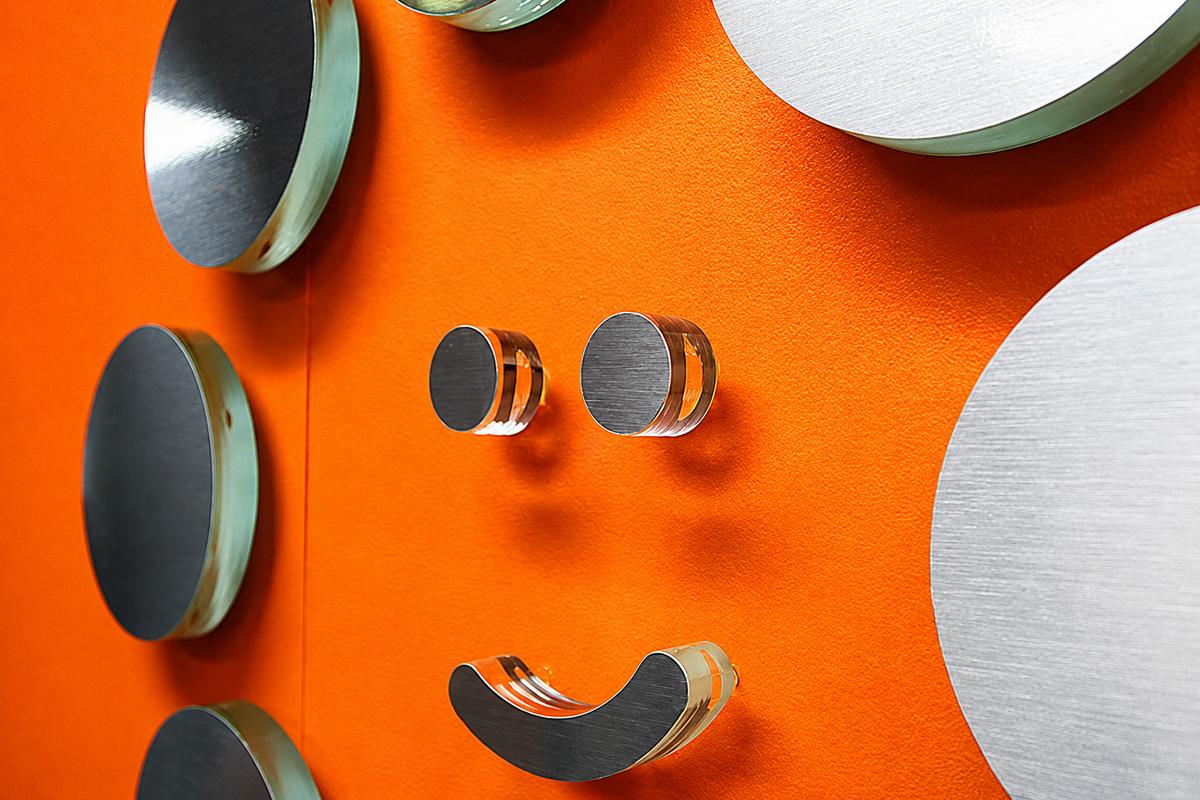 Close-up of SoftCom smile logo made from green edge acrylic with brushed metal faces and clear spacers on an orange wall