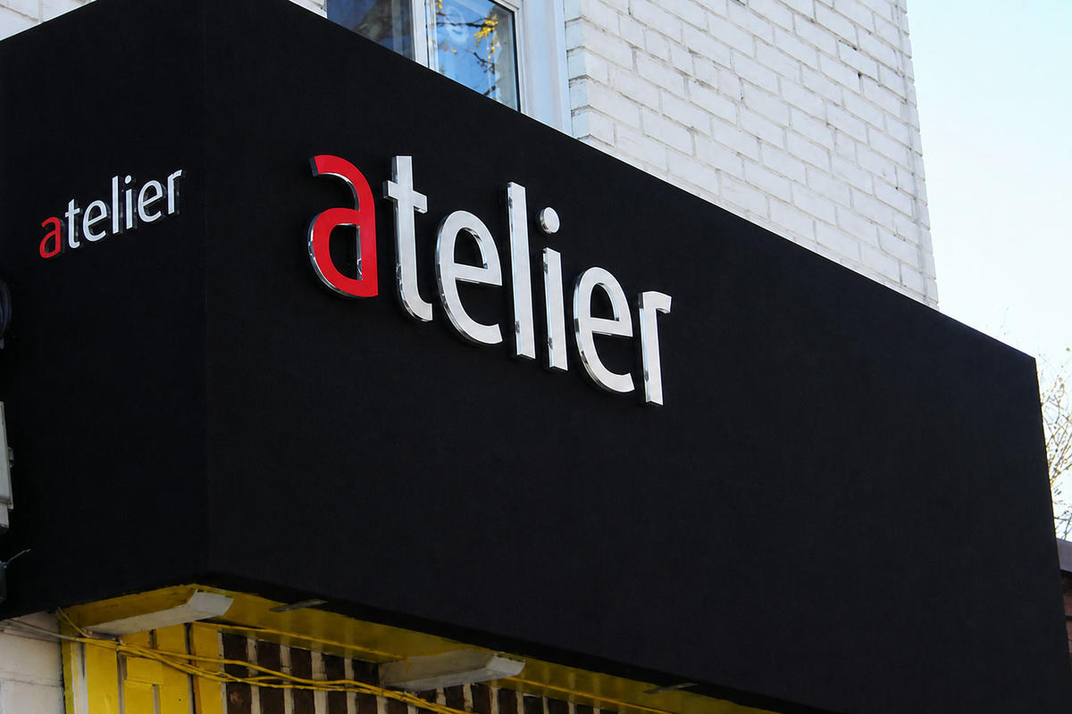 Angled view of Atelier projecting sign with two , 3 dimensional acrylic logos