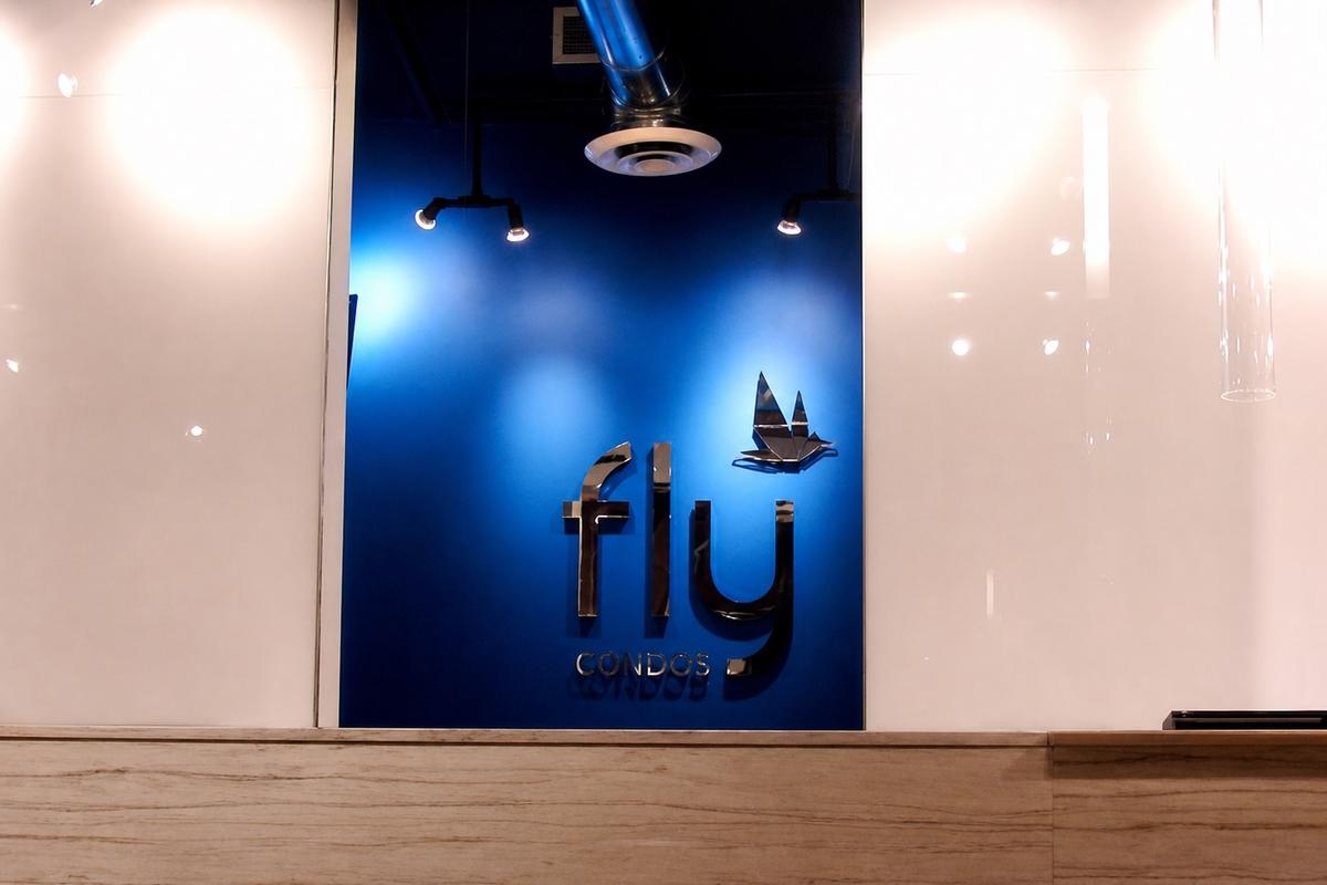 FLY Condos mirror acrylic logo on a blue sales centre feature wall