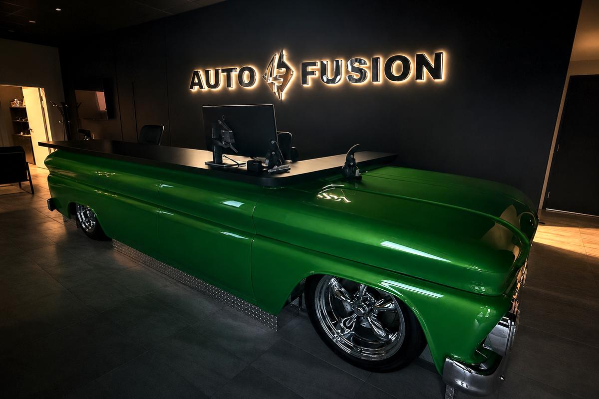 Backlit chrome Auto Fusion sign above a green classic pickup-truck reception desk in the showroom