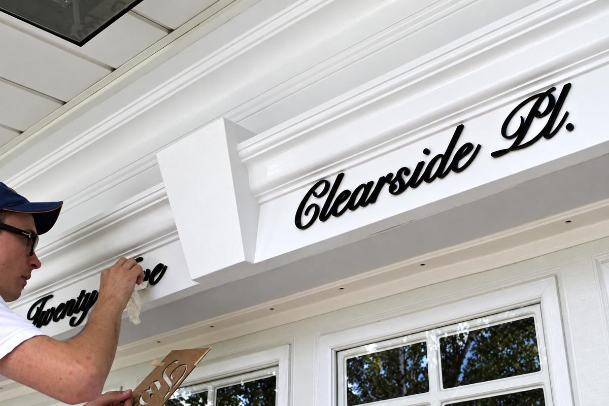 Installer applying black acrylic Twenty-Five and Clearside Pl. scripts above garage doors