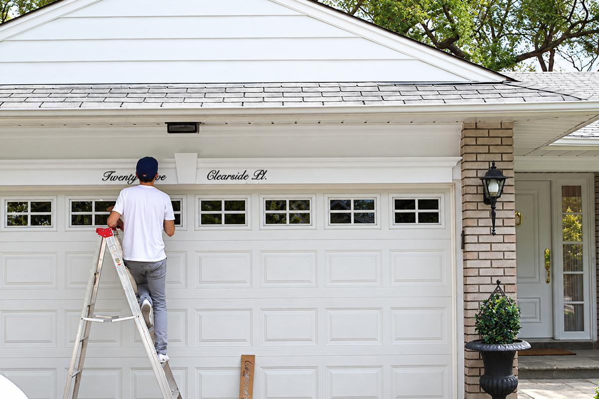 Installer mounting Twenty-Five and Clearside Pl. acrylic scripts above a residential garage