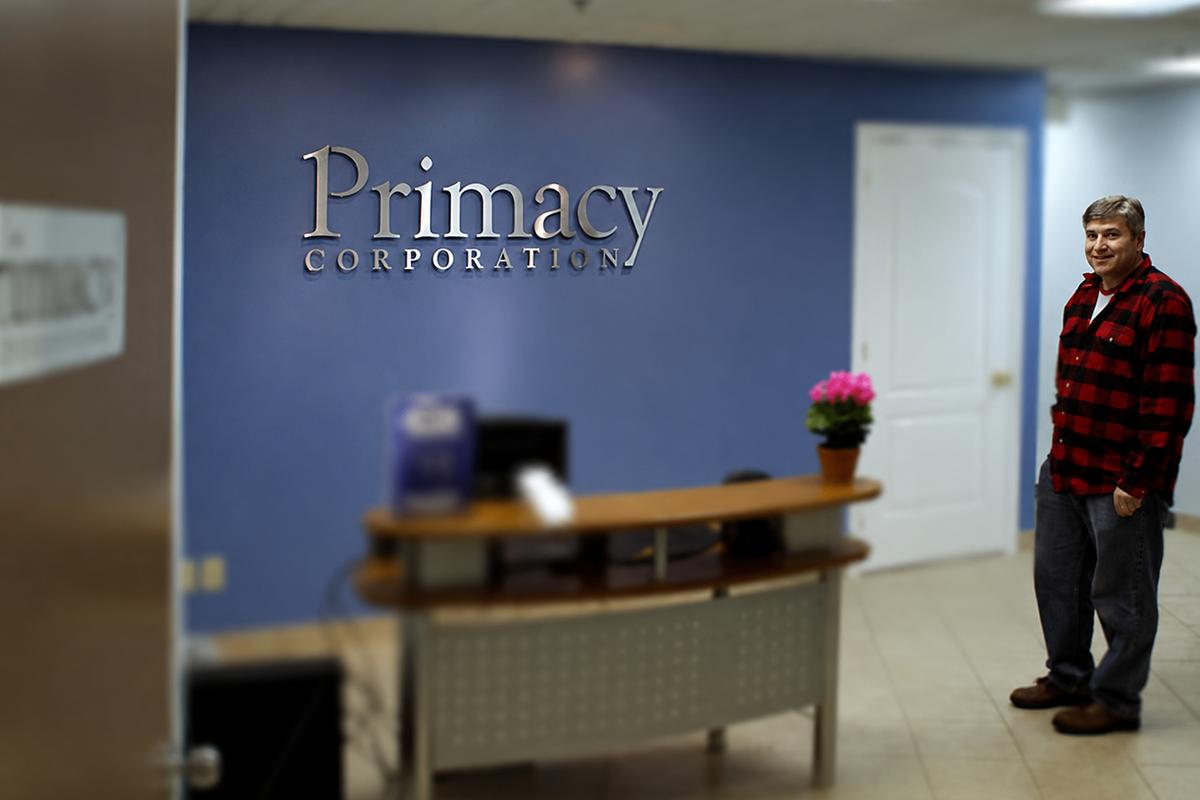Primacy Corporation dimensional acrylic logo sign installed behind a modern reception desk