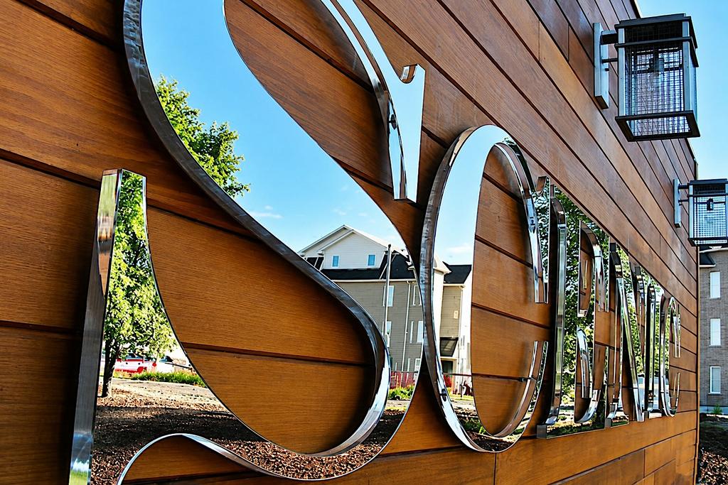 Angled view of SCENIC letters showing laminated second-surface mirror faces, polished clear edges and threaded-rod standoffs
